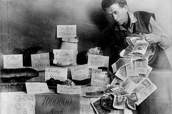 Um lojista faz-se retratar junto a uma montra com preços hiper inflacionados e um molho de notas. República de Weimar, Alemanha, anos 20.