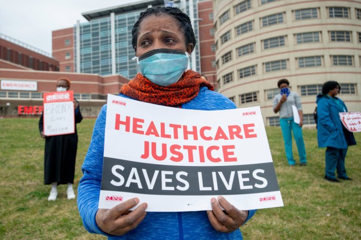A enfermeira Edith Ihejirika, empunhando um cartaz com os dizeres «Cuidados de saúde salvam vidas» foi uma das participantes num indignado protesto contra a falta de máscaras e luvas, realizado junto às urgências do Centro Médico Jacobi, no bairro do Bronx, em Nova Iorque, EUA, a 28 de Março de 2020