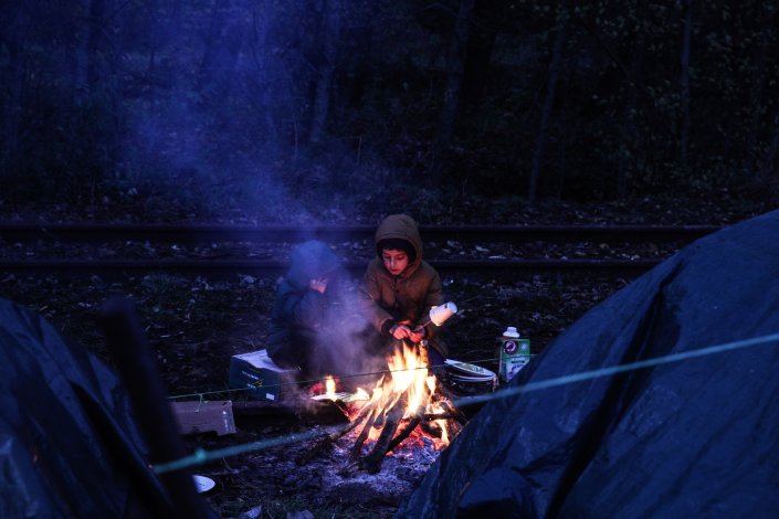 Criança migrante aquece-se junto a uma fogueira à entrada da sua tenda em Grande-Synthe, perto de Dunquerque, a 25 de Novembro de 2021. Mais de mil migrantes permanecem na costa francesa do Pas-de-Calais, esperando uma oportunidade de atravessar o Canal da Mancha em direcção ao Reino Unido