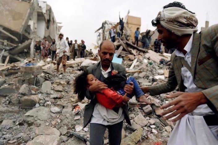 Um homen transporta uma criança ferida após um bombardeamento saudita no Iémen (imagem de arquivo)