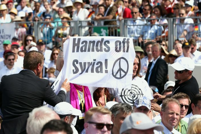 Um cartaz pelo fim dos ataques à Síria empunhado durante um discurso do antigo presidente norte-americano Barack Obama em Berlim (Alemanha). 19 de Junho de 2013