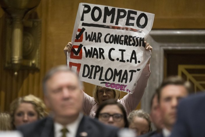 Uma manifestante segura um cartaz contra a designação do director da CIA, Mike Pompeo, para secretário de Estado dos EUA, durante a sua audição no Senado, em Washington, D.C.. 12 de Abril de 2018