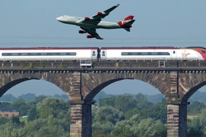 Avião sobrevoa comboio junto ao entroncamento de Weaver Junction, perto de Liverpool, Reino Unido 