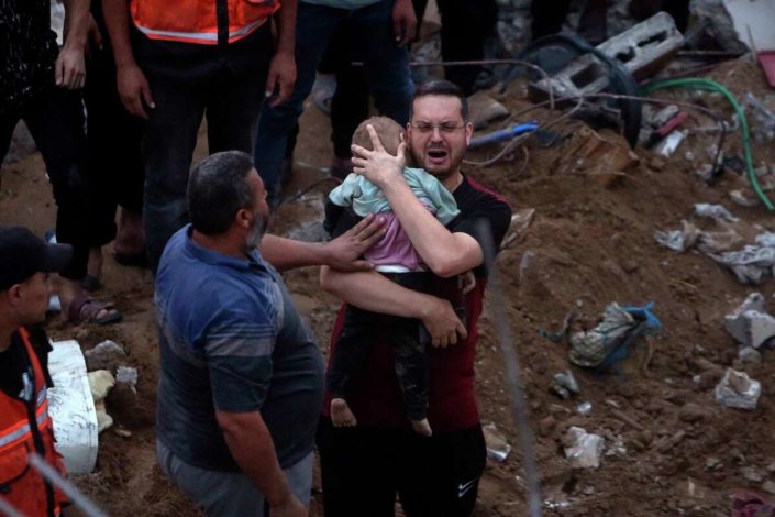 Um palestiniano chora com uma criança morta nos braços, entre as ruínas de um prédio atingido por bombas israelitas no campo de refugiados de Nusseirat, no centro da Faixa de Gaza, em 31 de Outubro de 2023 