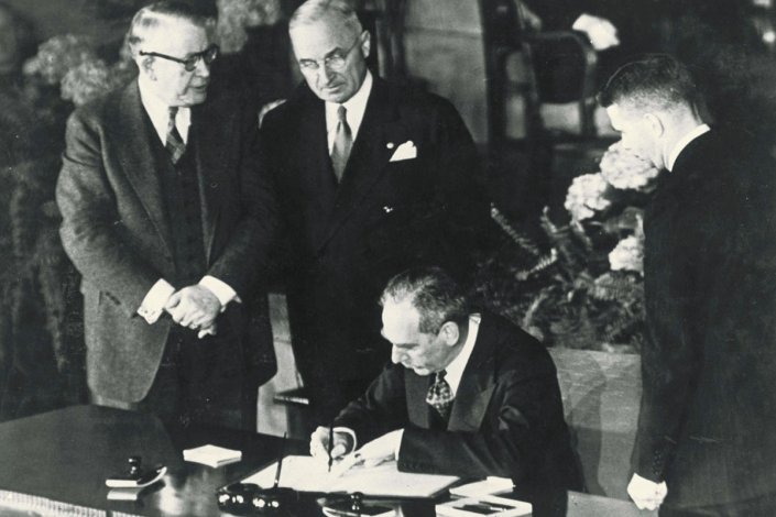 Harry Truman (no centro), presidente dos EUA, observa o secretário de Estado Dean Acheson, enquanto este assina o Tratado do Atlântico Norte, a 4 de Abril de 1949