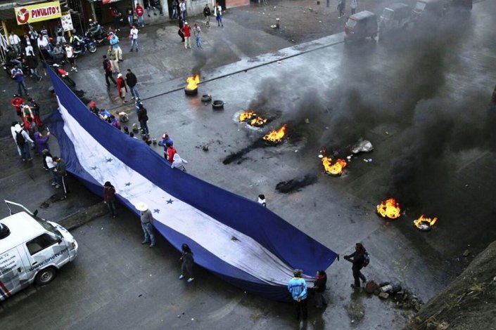 Manifestantes cortam estrada e estendem uma faixa com a bandeira das Honduras, durante a greve nacional iniciada no dia 20 de Janeiro