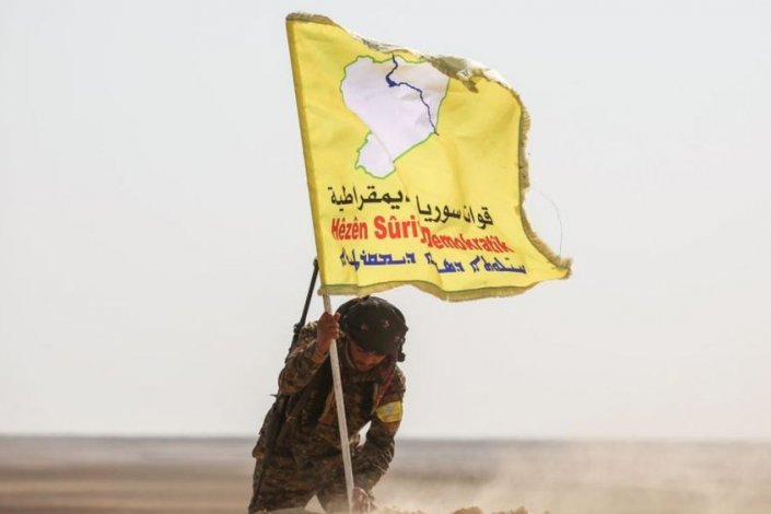 Um combatente das chamadas FDS fixa uma bandeira no chão perto de Raqqa (Fevereiro de 2017)
