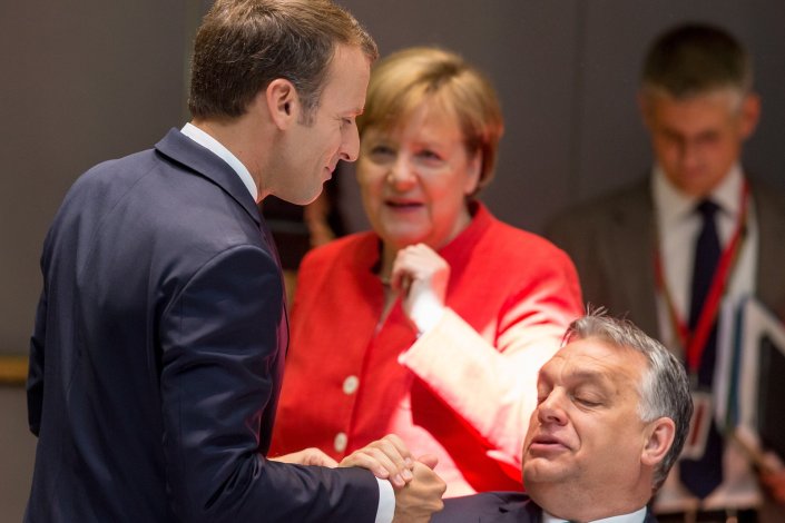 O presidente francês, Emmanuel Macron, cumprimenta o primeiro-ministro húngaro, Viktor Orban, sob o olhar da chanceler alemã, Angela Merkel, durante a reunião do Conselho Europeu. 29 de Junho de 2018