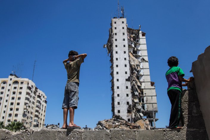 Crianças palestinianas olham para um edifício destruído em na Cidade de Gaza na sequência de ataques aéreos israelitas